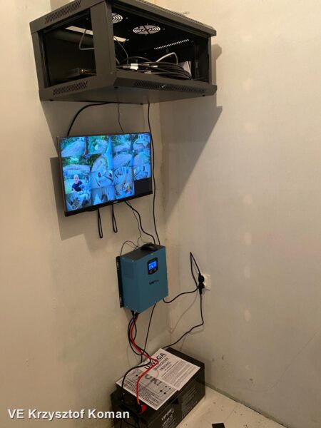 Szafa rack z rejestratorem i switchem PoE, monitor z podglądem kamer IP, przetwornica i akumulator kwasowy 12 V — centrum systemu monitoringu z zasilaniem awaryjnym
